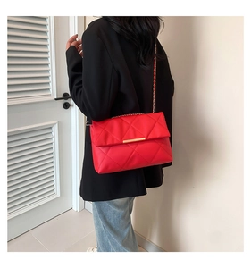 Detail view of bright red quilted shoulder bag with metal chain strap and turn-lock closure