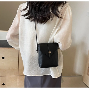 Detail of black pebbled leather crossbody bag with gold buckle on a shoulder model