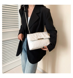 White quilted crossbody bag with gold chain strap worn with a black blazer and denim