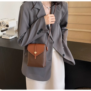 Detail of a brown patchwork crossbody phone bag with gold clasp on a model in a cafe