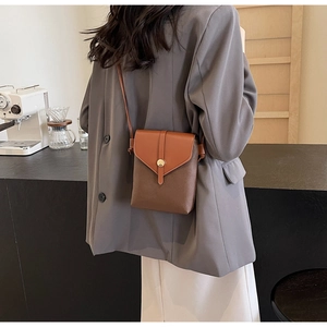 Detail view of a small two-tone leather crossbody phone bag with gold metal round clasp