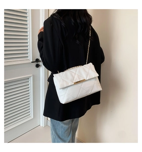 Detail of white quilted crossbody bag with gold chain strap and metal lock closure