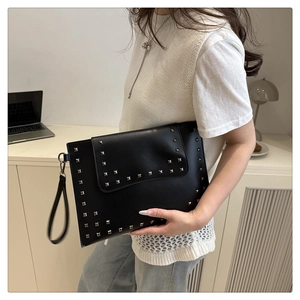Detail of a black envelope clutch with silver square studs and leather wristlet strap
