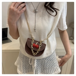 Detail of a mini brown leather crossbody bag with 3D cherry accent and gold chain strap