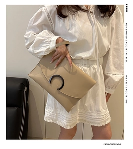 Detail of minimalist beige envelope clutch bag with C-ring buckle held by a model