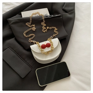 Flat lay of a white saddle bag with red cherry charm and dual gold chain straps