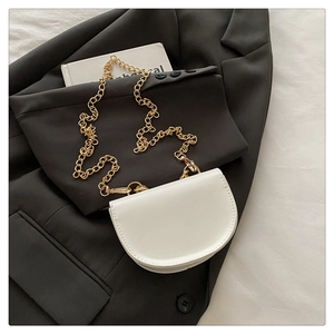 Detail of white mini saddle bag with gold chain strap on black blazer background