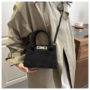 Detail of black suede trapezoid handbag with gold lock and thin strap in lifestyle setting