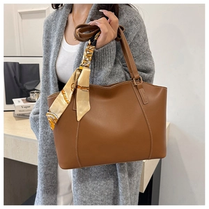 Detail of a brown leather tote bag with a decorative silk scarf wrapped on the handle