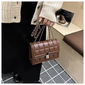 Detail of chocolate brown quilted crossbody bag with silver chain strap and square metal lock