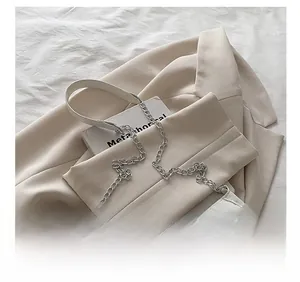 Detailed view of white pleated shoulder bag with chain and leather strap on beige blazer