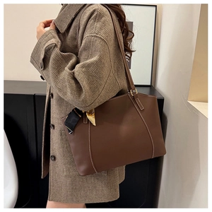 Detail of dark brown tote bag featuring white contrast stitching and a silk scarf handle