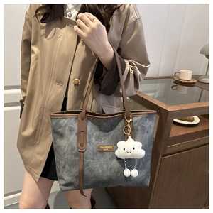 Detail of grey tote bag with brown leather trim and fluffy white cloud charm accessory