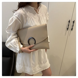 Detail of a minimalist apricot envelope clutch with a crescent metal buckle and hand strap