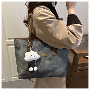 Detail of grey-blue canvas tote bag with brown leather handles and plush cloud charm