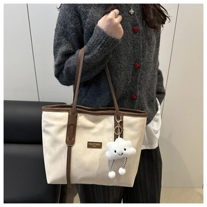 Detail of canvas tote bag with brown leather handles and a plush cloud charm accessory