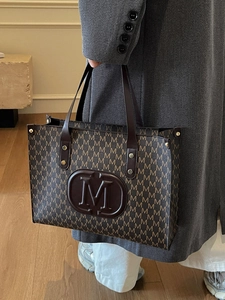 Elegante braune Vintage-Einkaufstasche mit M-Muster und Ledergriffen in stilvoller Umgebung