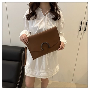 Detail of caramel brown envelope clutch featuring a metal crescent moon buckle and wrist strap