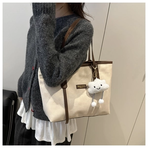 Detail of cream tote bag with brown straps, logo plate and plush cloud pendant charm