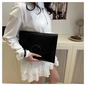 Detail of a black envelope clutch bag with metal ring buckle shown with a lace outfit