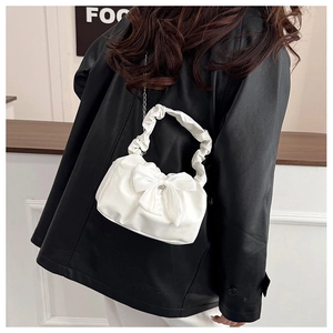 Close-up of white ruched handbag with large bow and elegant metal chain strap for women