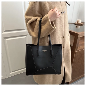 Detail of a large black leather tote bag featuring elegant stitching and a long handle