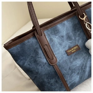 Detailed close-up of blue denim tote bag with leather trim and plush ball keychain