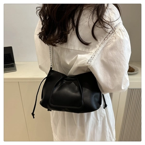 Detalle de bolso bandolera negro con cordón, cadena metálica y acabado en cuero con pliegues