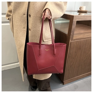 Detail of red large tote bag with geometric stitching and golden brand logo on matte leather