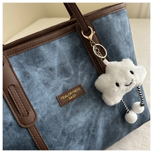 Close-up of blue denim tote bag with brown leather trim and a white cloud plush charm
