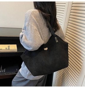 Close-up of black suede tote bag with golden twist lock and leather shoulder straps