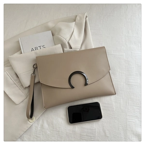 Detail shot of beige envelope clutch with crescent metal buckle and wrist strap