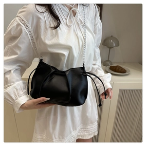 Detail of black pleated tote bag with silver chain strap and drawstring design on a model
