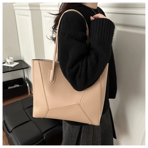 Detail of light beige tote bag with geometric stitching shown on shoulder by model