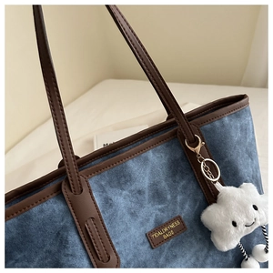 Close-up of blue denim tote bag with brown leather trim and cute white cloud charm