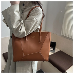 Detail of caramel brown leather tote featuring asymmetric geometric seams and slim handles