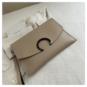 Detail view of beige envelope clutch with C-shape metal buckle and wristlet strap