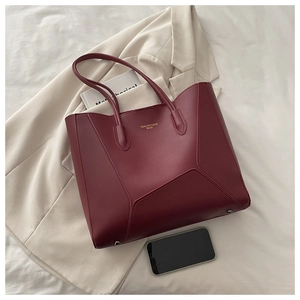 Detail view of burgundy leather tote bag featuring gold logo and bottom metal feet