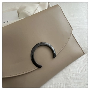 Detail of khaki envelope clutch with a glossy C-shaped buckle and fine stitching