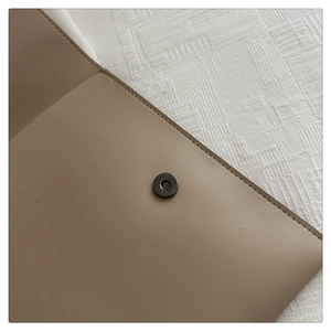 Detailed close-up of the magnetic buckle and fine stitching on a khaki leather envelope bag