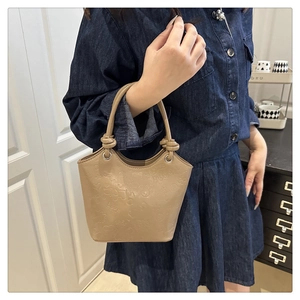 Detail of khaki textured bucket bag featuring embossed letters and knotted top handle strap