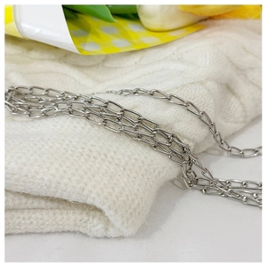 Détail d'une chaîne métallique argentée multicouche sur un fond en tricot blanc doux