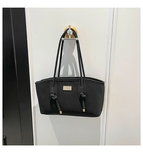 Detail of black quilted tote bag with metallic plaque and stylish knotted shoulder straps