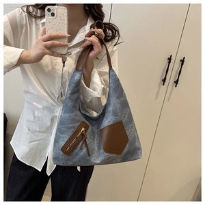 Detail of blue denim hobo bag featuring brown leather pockets and tassel zip accents