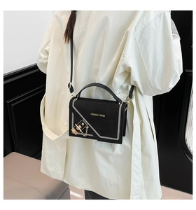 Detail of black crossbody bag featuring contrast white stitching and gold lock hardware