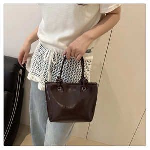 Detail of a dark brown glossy patent leather tote bag with unique knotted handle design