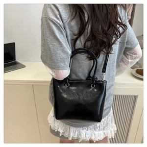 Détail d'un sac à main noir en cuir verni porté par un mannequin pour illustrer la taille