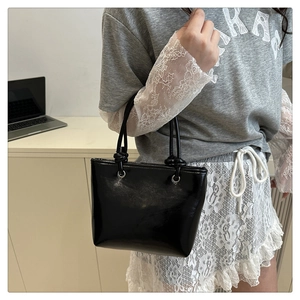 Detail of black glossy bucket bag featuring elegant knot strap design and shiny finish