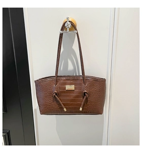 Detailed close-up of dark brown crocodile texture leather and gold logo plaque on a tote bag