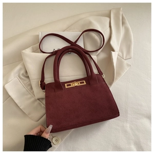 Dettaglio borsa in pelle scamosciata bordeaux con chiusura dorata su giacca bianca